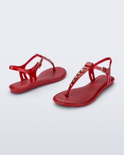 Angled view of a pair of red Solar Boho t-strap sandals with ,metallic detailing on the front strap