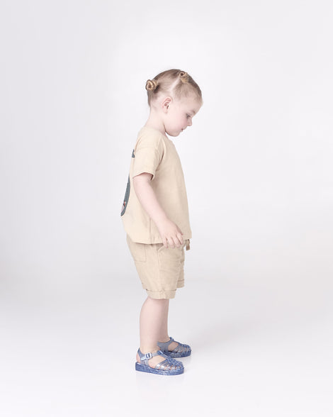 A model posing wearing a pair of Mini Melissa Possession baby sandals in glitter blue with velcro buckle closure on the ankle straps