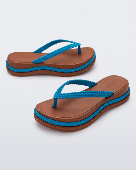 An angled front and side view of a pair of brown/blue Melissa Leblon platform flip flops with details that mimic sisal braids on the sole and strap