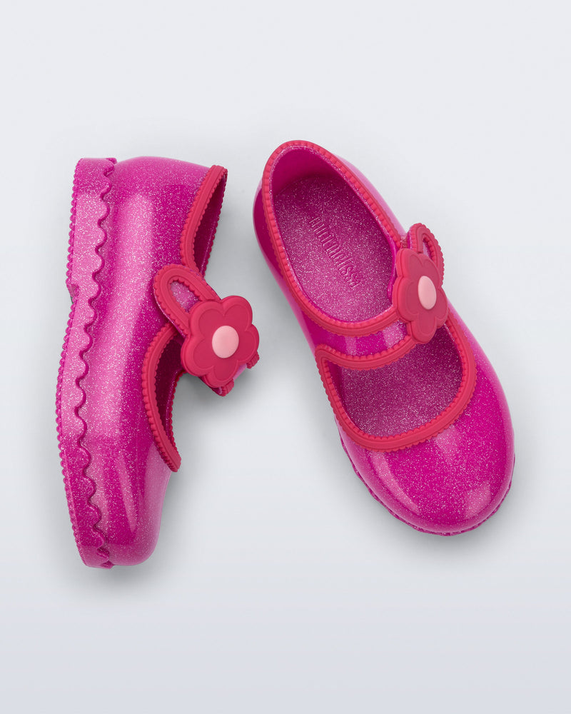 Side and top view of a pair of glitter pink Hip Ballerina baby flats with flower on strap