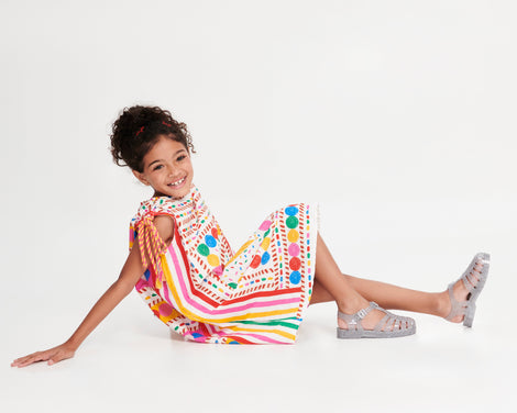 Child model in a multi colored dress wearing a pair of glitter/clear/silver Possession kids fisherman sandals