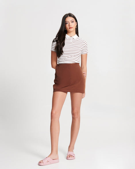 Model in a brown skirt and white stripped shirt wearing a pair of pink Cozy Cross sandals with crisscross top straps