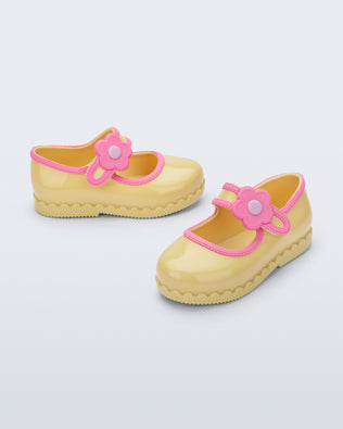 Side and angled view of a pair of yellow Hip Ballerina baby flats with flower on strap and pink trim