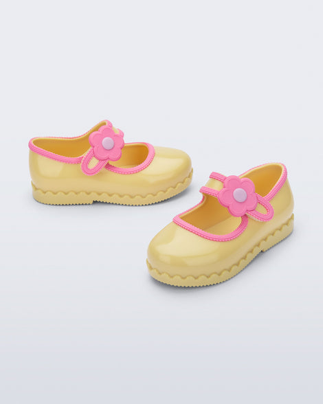 Side and angled view of a pair of yellow Hip Ballerina baby flats with flower on strap and pink trim