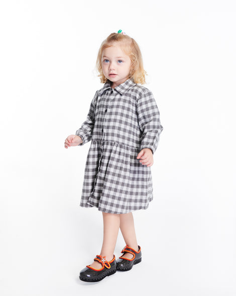 Child model in a black and white checkered dress wearing a pair of glitter black Hip Ballerina Star baby flats with star on upper strap