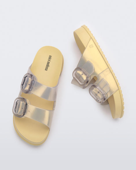 A top and side view of a pair of pearly yellow Mini Melissa Cozy slides with two front straps with buckle details