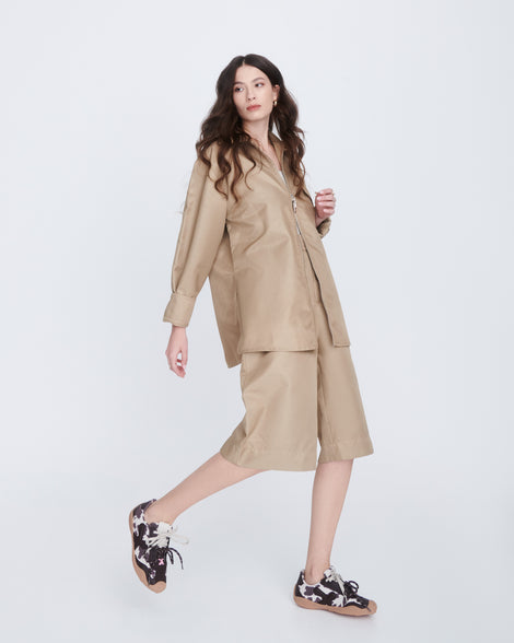 Model in a beige outfit wearing a pair of black and white cow print X Bend sneakers with beige sole