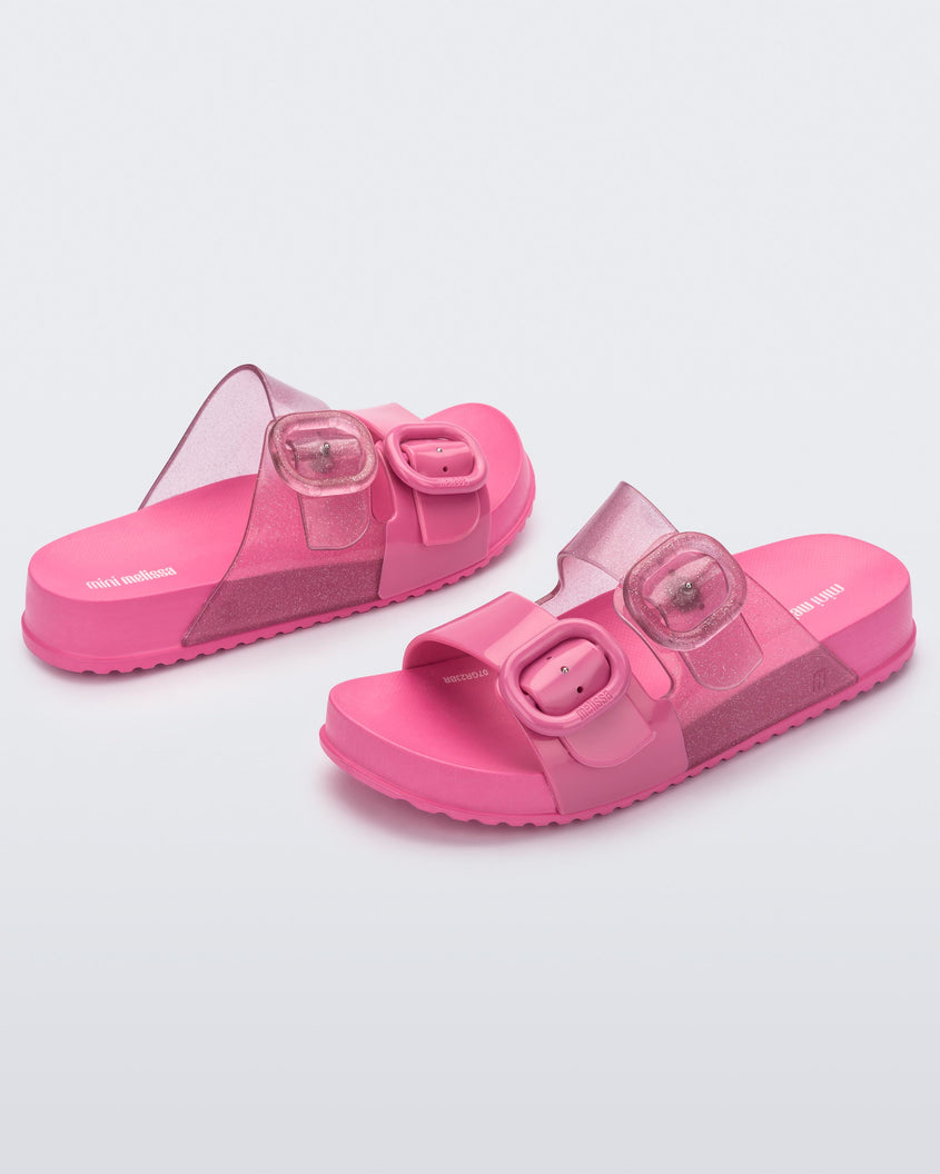 An angled front and side view of a pair of pink Mini Melissa Cozy slides with two front straps with buckle details