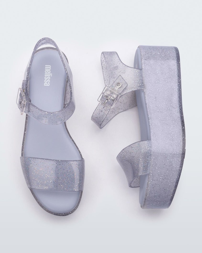 An angled top and side view of a pair of glitter lilac Melissa platform sandals with a front and ankle strap
