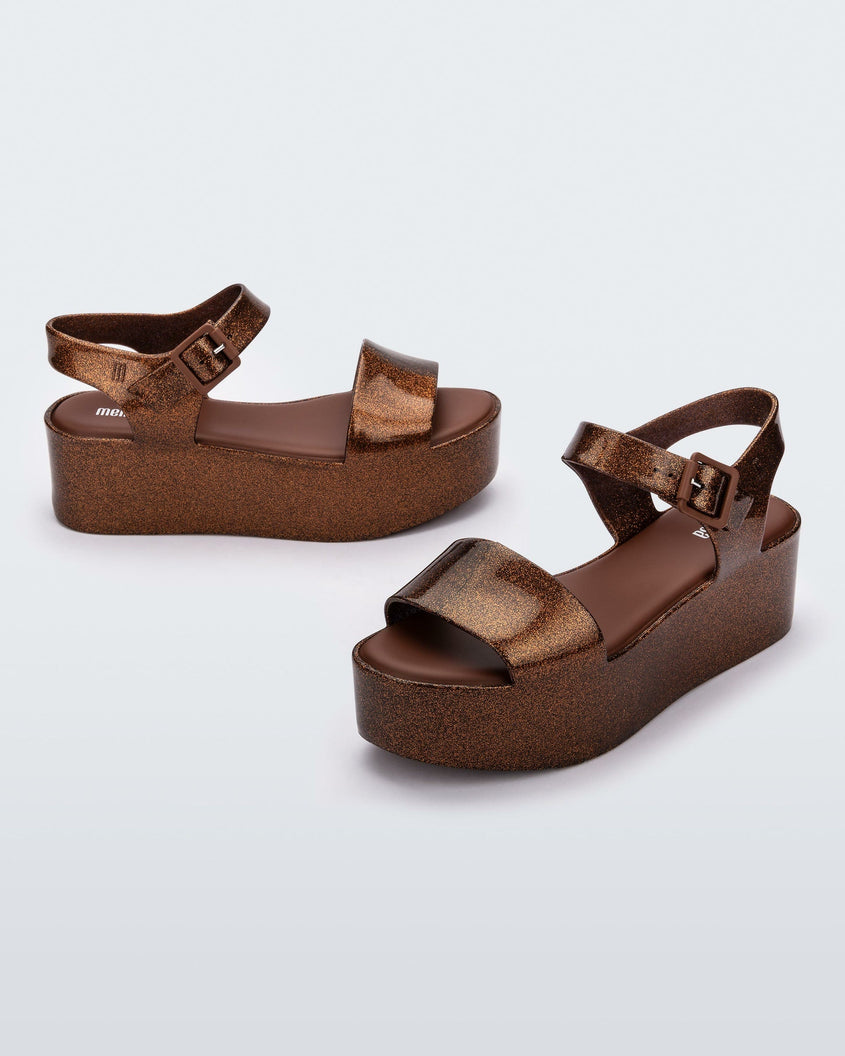 An angled front and side view of a pair of bronze Melissa platform sandals with a front and ankle strap