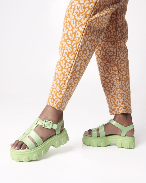 Model's legs in orange patterned pants wearing a pair of green Ella platform sandals