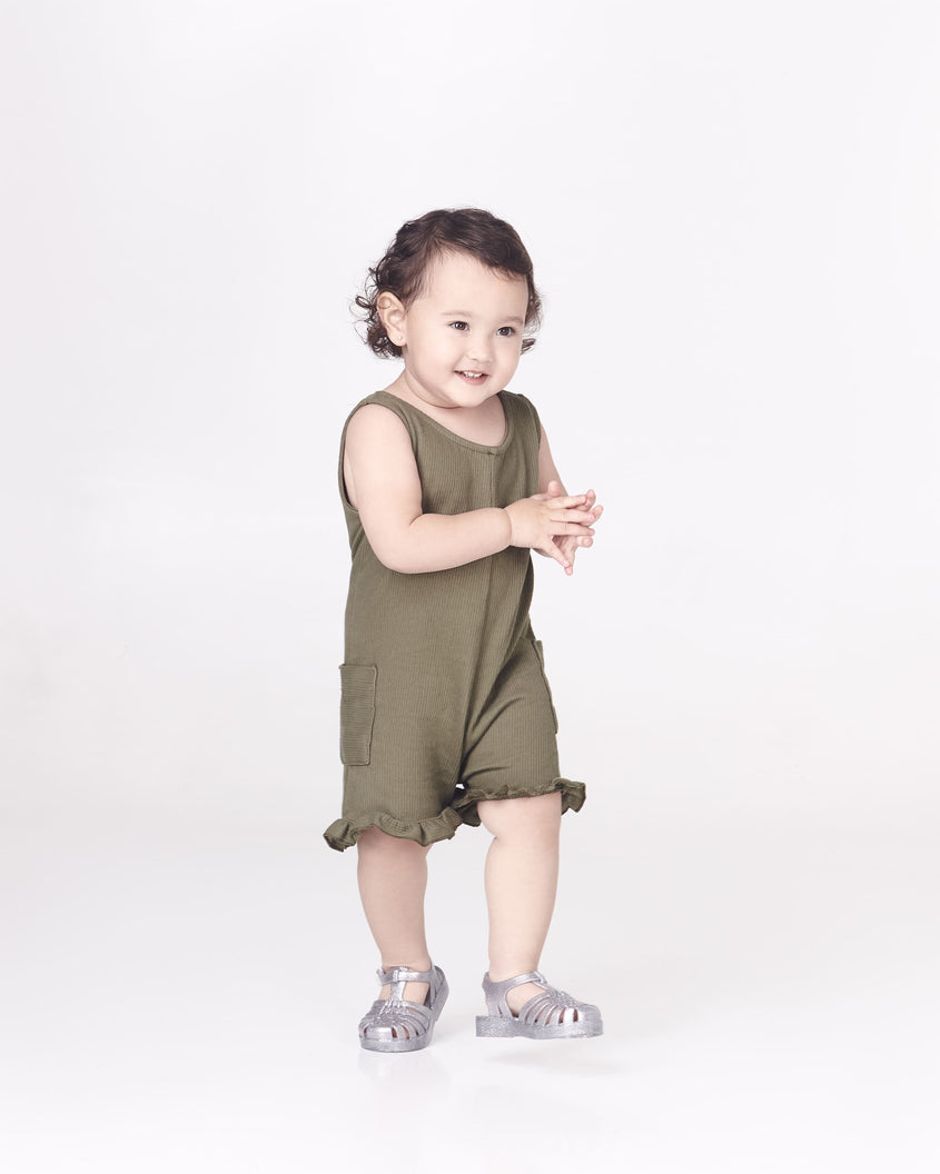 A model posing wearing a pair of Mini Melissa Possession baby sandals in glitter clear with velcro buckle closure on the ankle straps