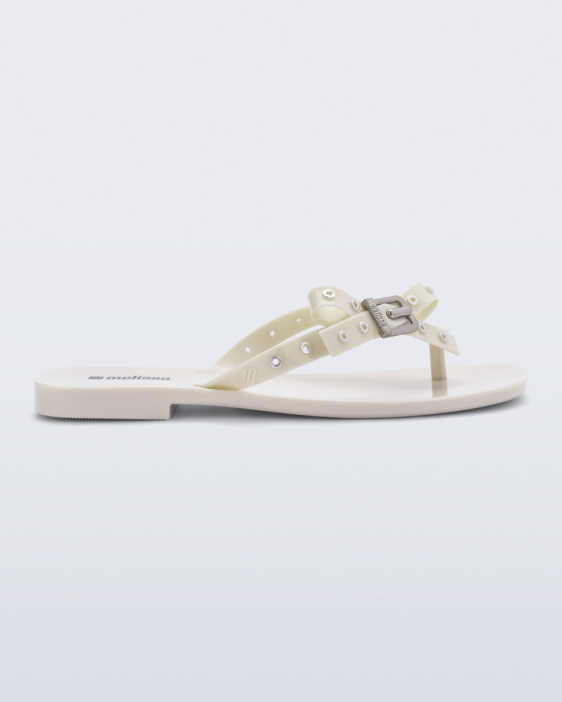 Side view of a beige Harmonic Squared flip flop with bow on strap