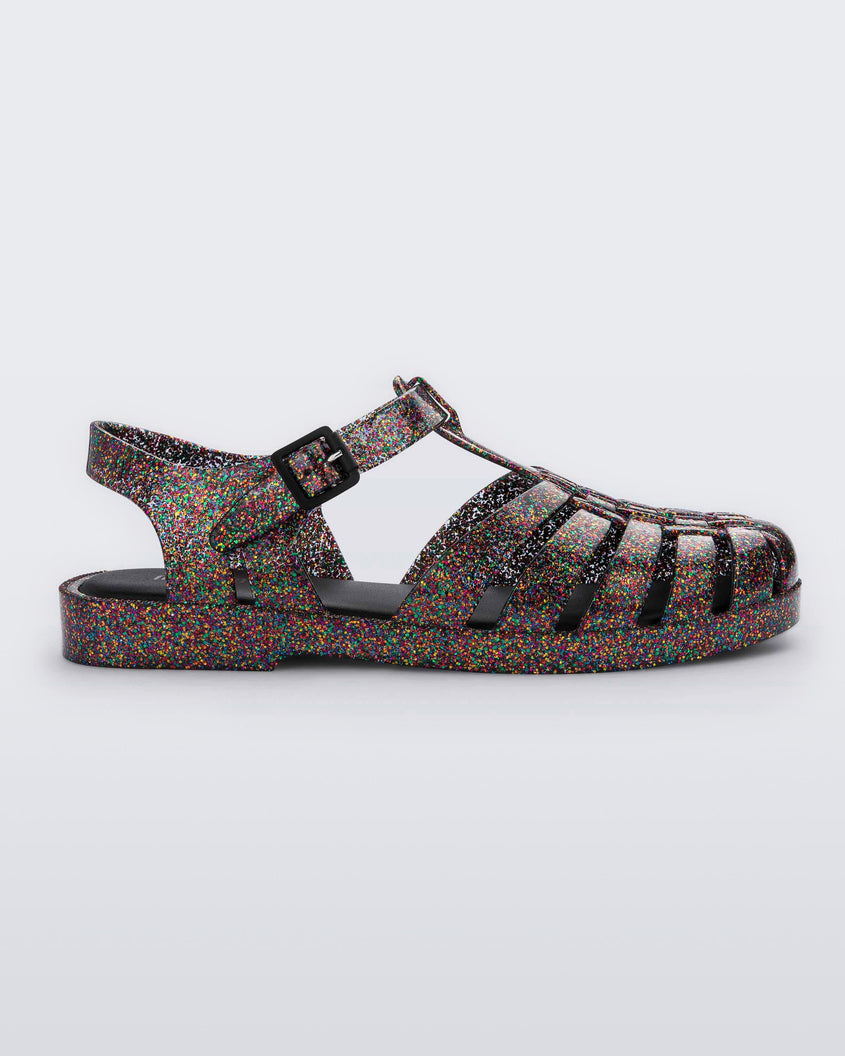 Side view of a multicolored glitter Melissa Possession sandal with a closed toe front weft design connected to a top strap with a buckle.