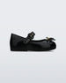 An outter side view of a black Mini Melissa Sweet Love flat with a top strap and a bow detail on the toe.