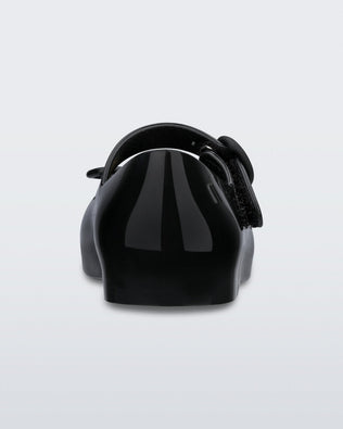 Back view of a black Mini Melissa Sweet Love flat with a top strap and a bow detail on the toe.