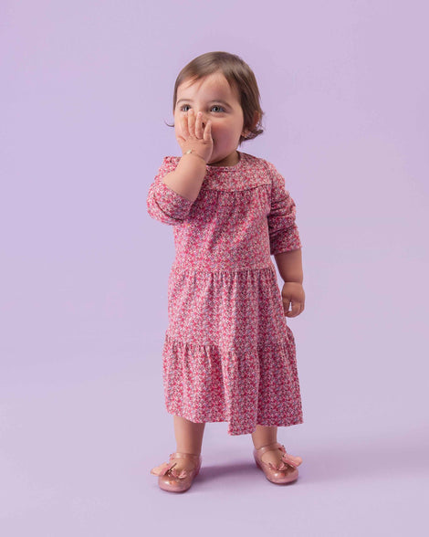 A toddler in a pink floral dress wearing a pair of glitter clear pink Mini Melissa Ultragirl Butterfly baby mary jane flats with two pink metallic and clear butterflies and peep toe.