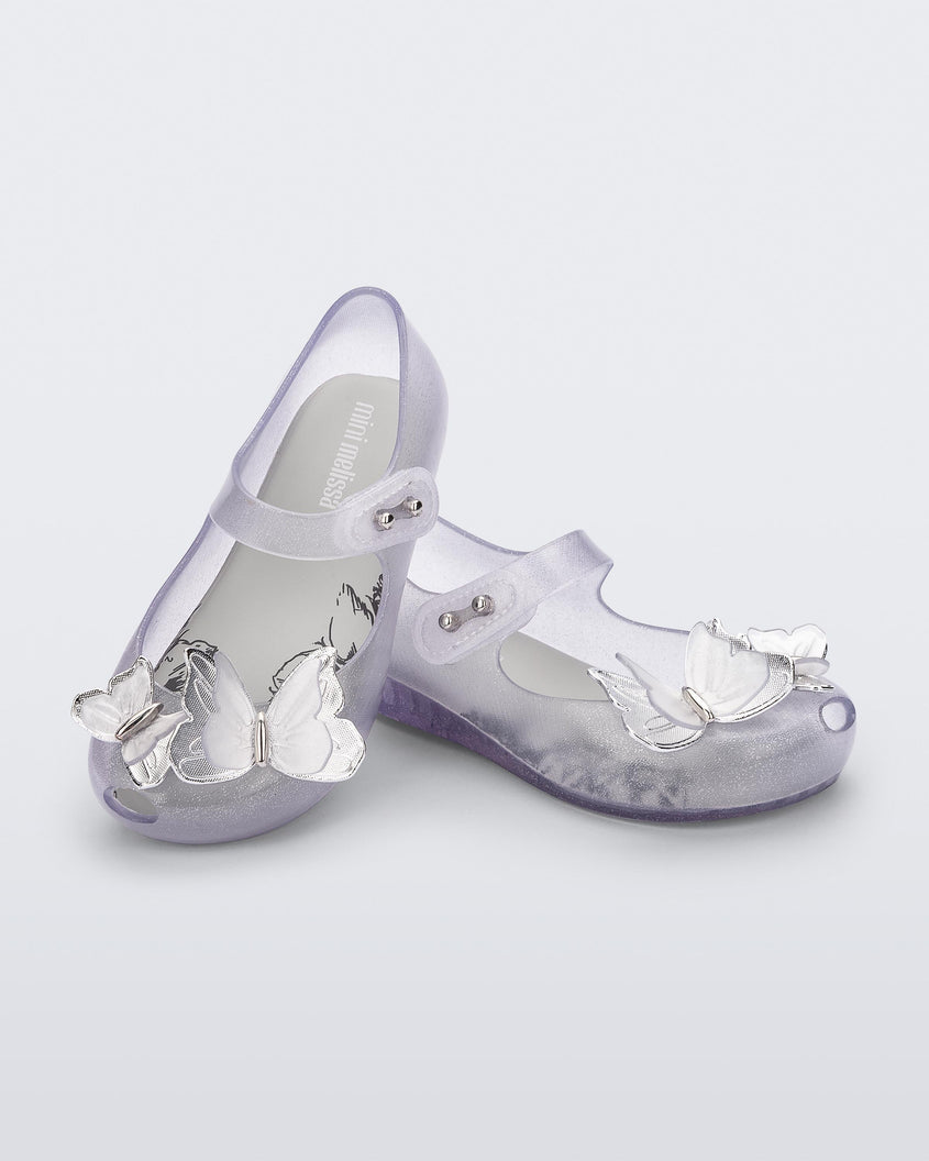 Angled view of a pair of clear glitter Mini Melissa Ultragirl Butterfly baby mary jane flats with two metallic and clear butterflies and peep toe.