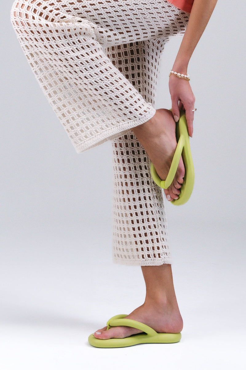A model's legs in white pants wearing a pair of lime green Melissa Free Flip Flops with puffer-like straps.