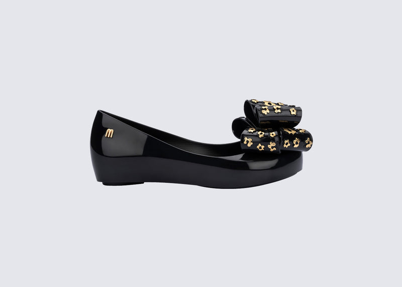 Side view of a black Ultragirl Sweet X kids flats with a bow that has chrome flowers on it