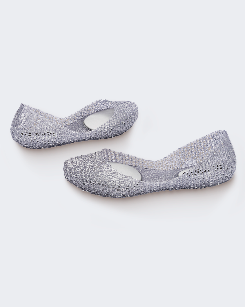 An angled side and back view of a pair of glitter silver Melissa Campana flats with a distinctive interwoven pattern