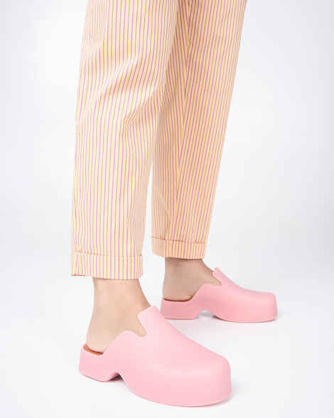 Model's legs wearing a pair of pink Melissa Zoe mules with orange insoles.