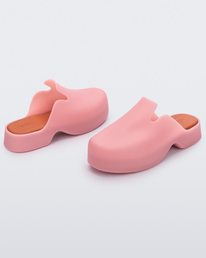 Angled view of a pair of pink Melissa Zoe mules with orange insoles.