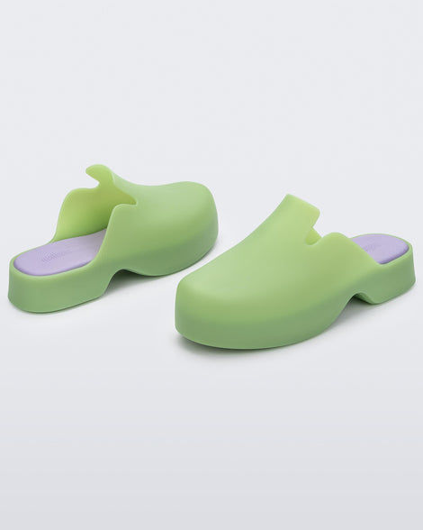 Angled view of a pair of green Melissa Zoe mules with purple insoles.