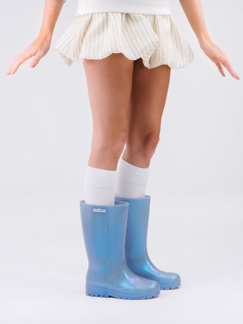 Model's legs in a beige skirt wearing a pair of pearly blue Welly rain boots with knee high socks