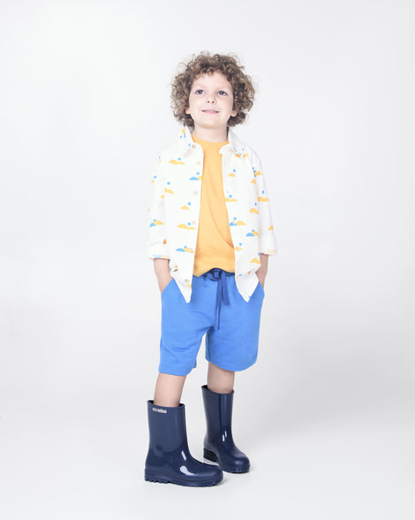 A child model in blue shorts wearing a pair of blue Melissa Welly boots.