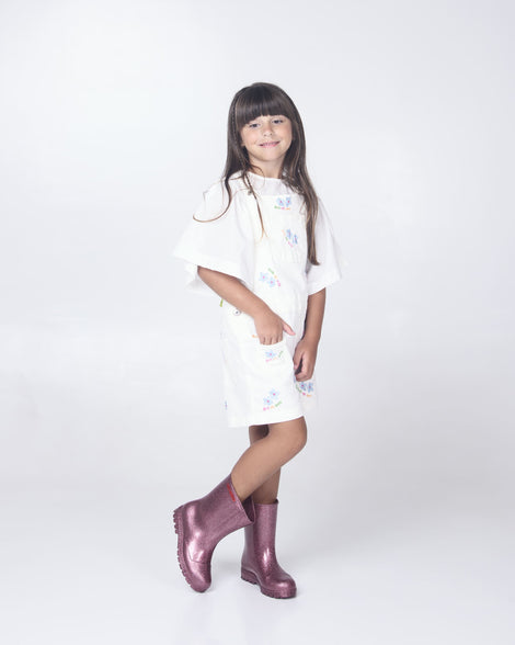 A child model in a white dress wearing a pair of glitter pink Melissa Welly boots.