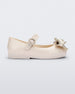 Side view of a beige Mini Melissa Sweet Love baby mary jane flat with a metallic gold bow.