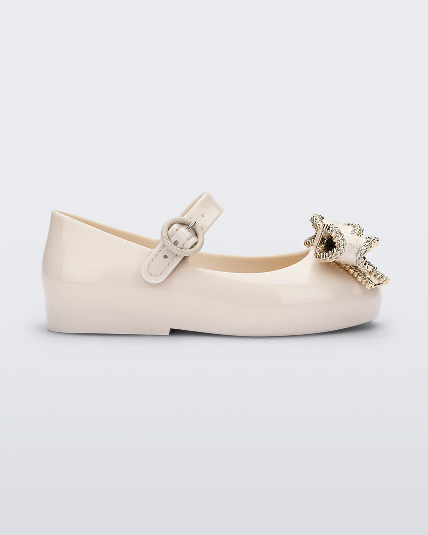 Side view of a beige Mini Melissa Sweet Love baby mary jane flat with a metallic gold bow.