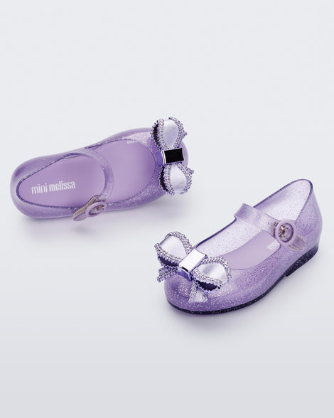 Top and angled view of a pair of lilac Mini Melissa Sweet Love baby mary jane flats with a metallic lilac bow.