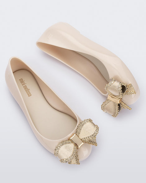 Side and angled view of a pair of beige Mini Melissa Sweet Love kids flats with gold bow.