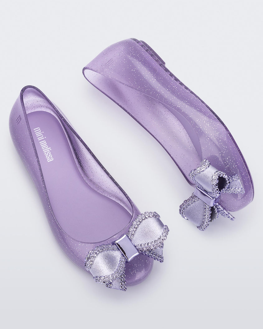 Side and angled view of a pair of lilac Mini Melissa Sweet Love kids flats with metallic lilac bow.