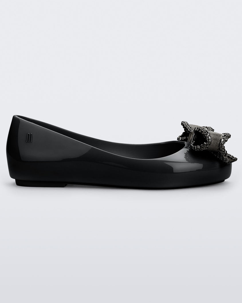 Side view of a black Mini Melissa Sweet Love kids flat with a metallic gray bow.
