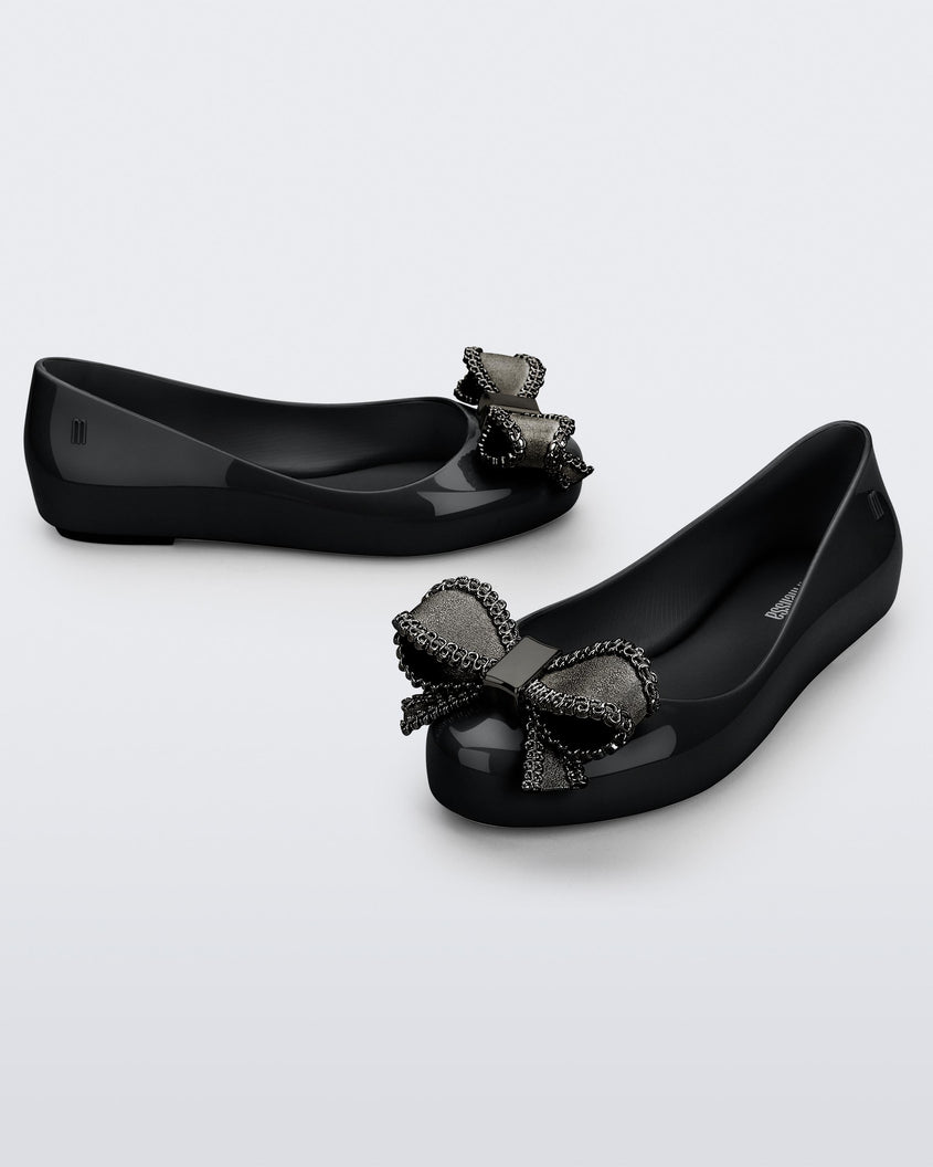 Side and angled view of a pair of black Mini Melissa Sweet Love kids flats with metallic gray bow.