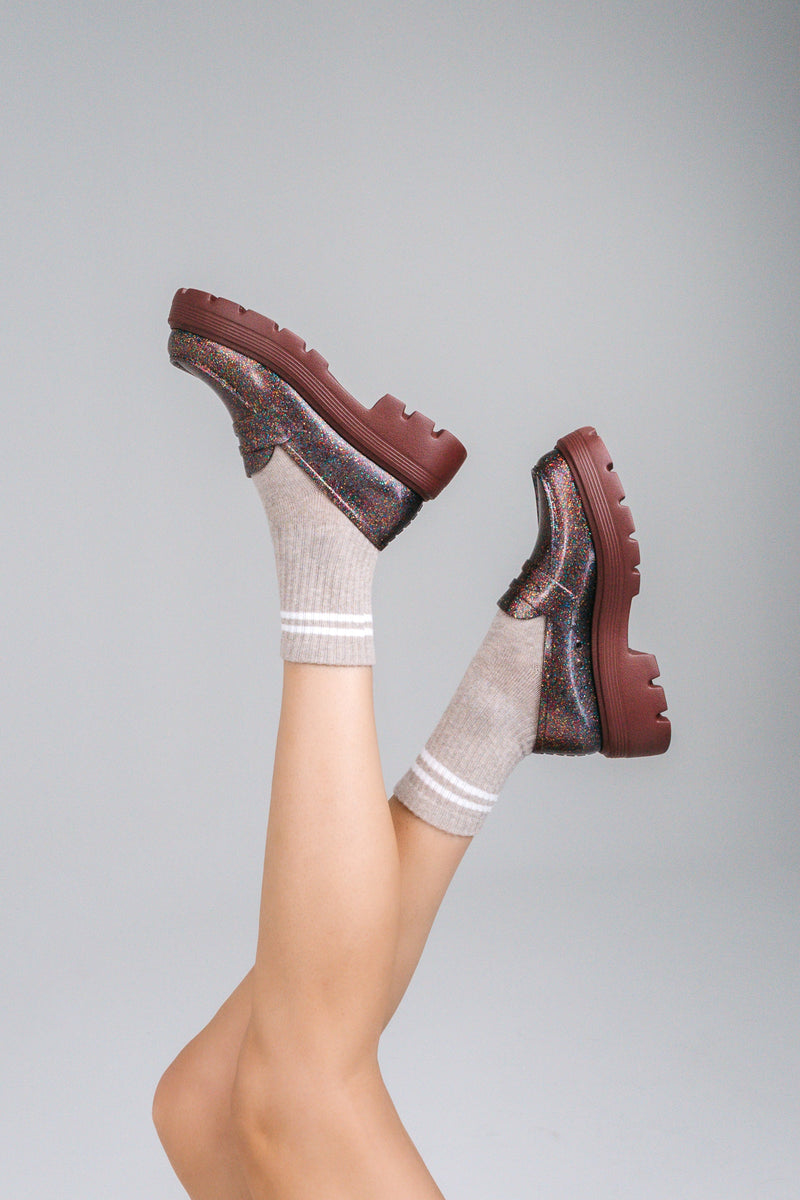 Model's legs in beige socks wearing a pair of  Melissa Royal loafers in glitter multicolor with a brown platform sole.