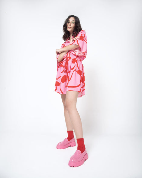 A model posing in a patterned dress wearing a pair red ankle socks and the Melissa Royal platform loafers in Pink