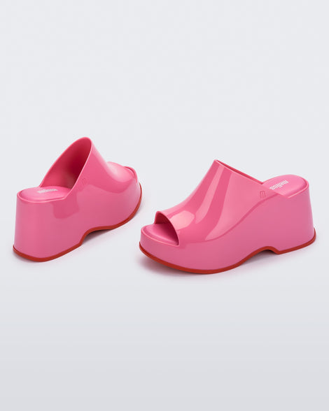 Angled view of a pair of pink Melissa Patty platform mules with red outsoles.