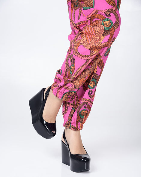 A model's legs in pink print pants wearing a pair of black Melissa Groovy wedge platform slingback heels with peep toe.