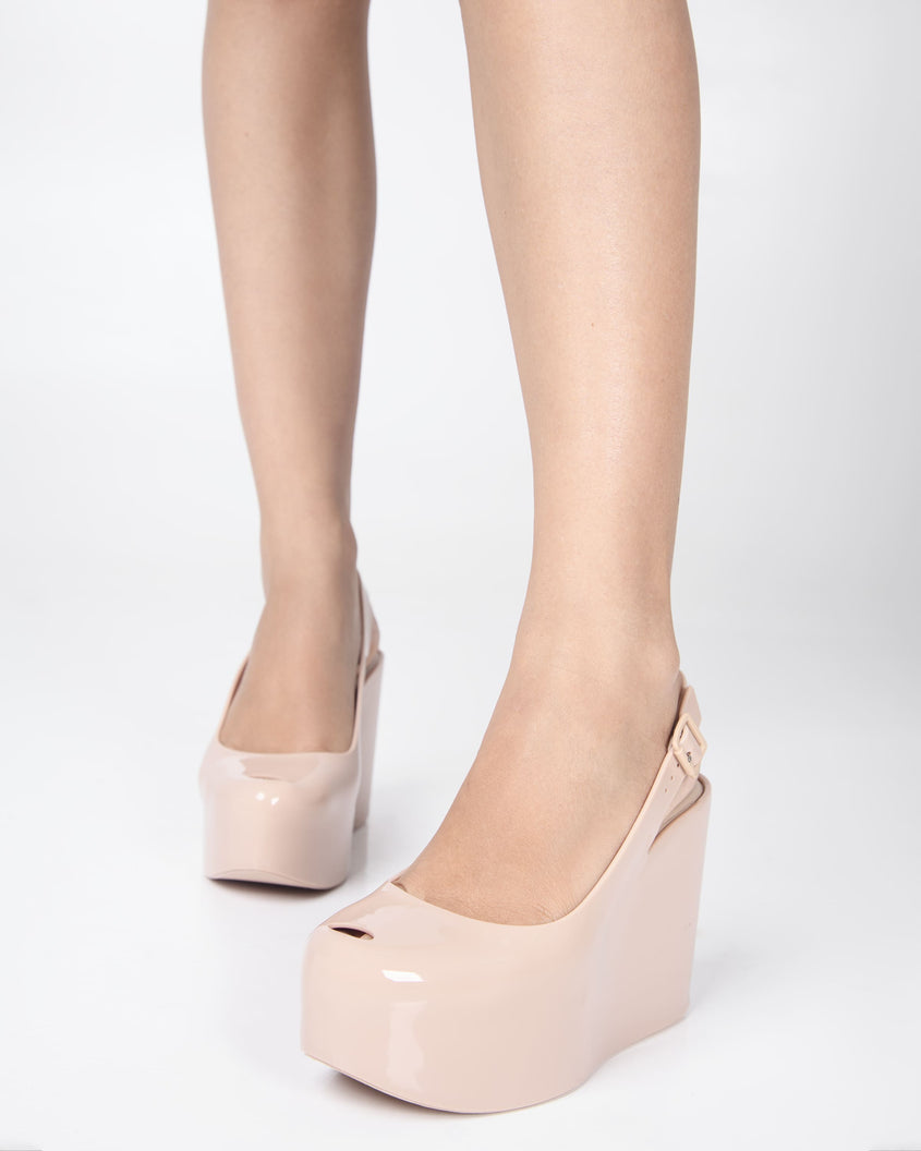 A model's legs wearing a pair of beige Melissa Groovy wedge platform slingback heels with peep toe.