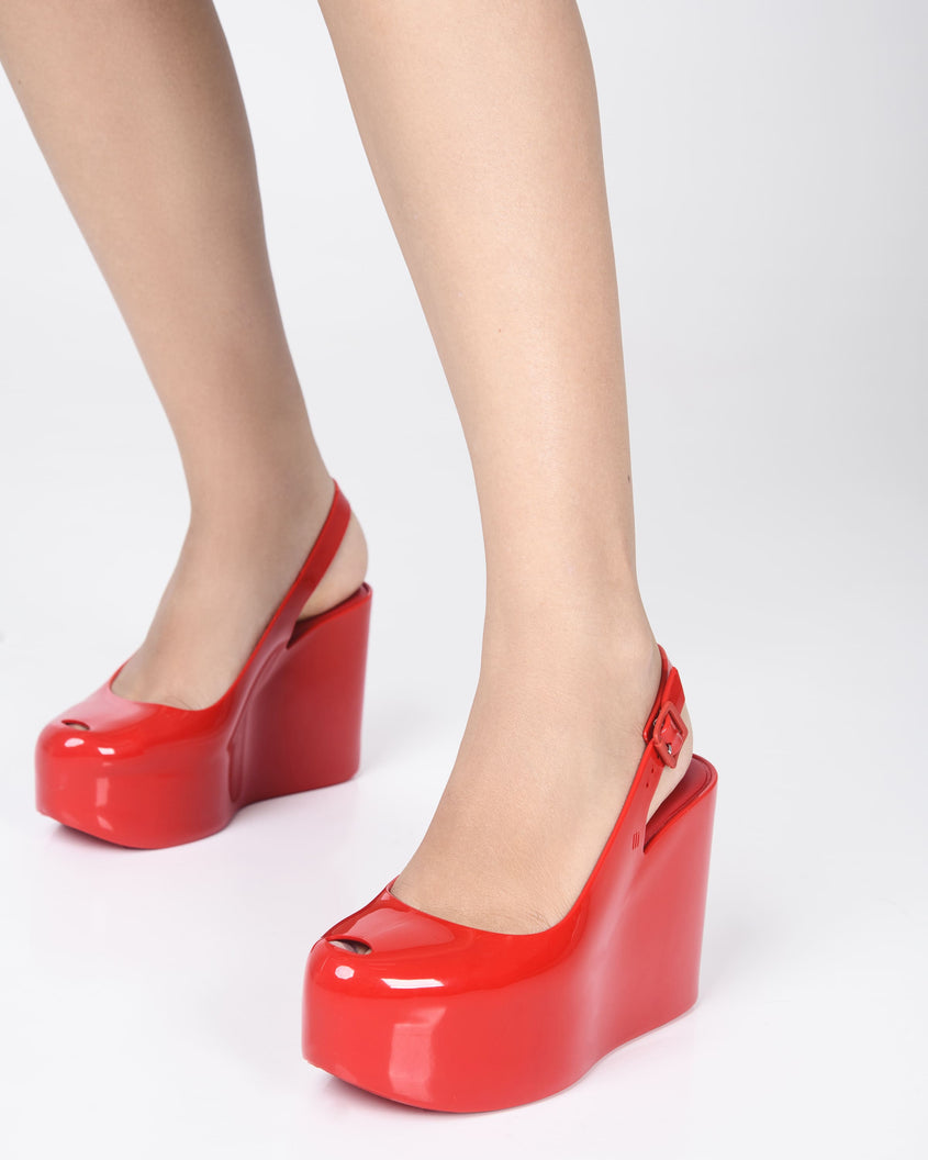 A model's legs wearing a pair of red Melissa Groovy wedge platform slingback heels with peep toe.