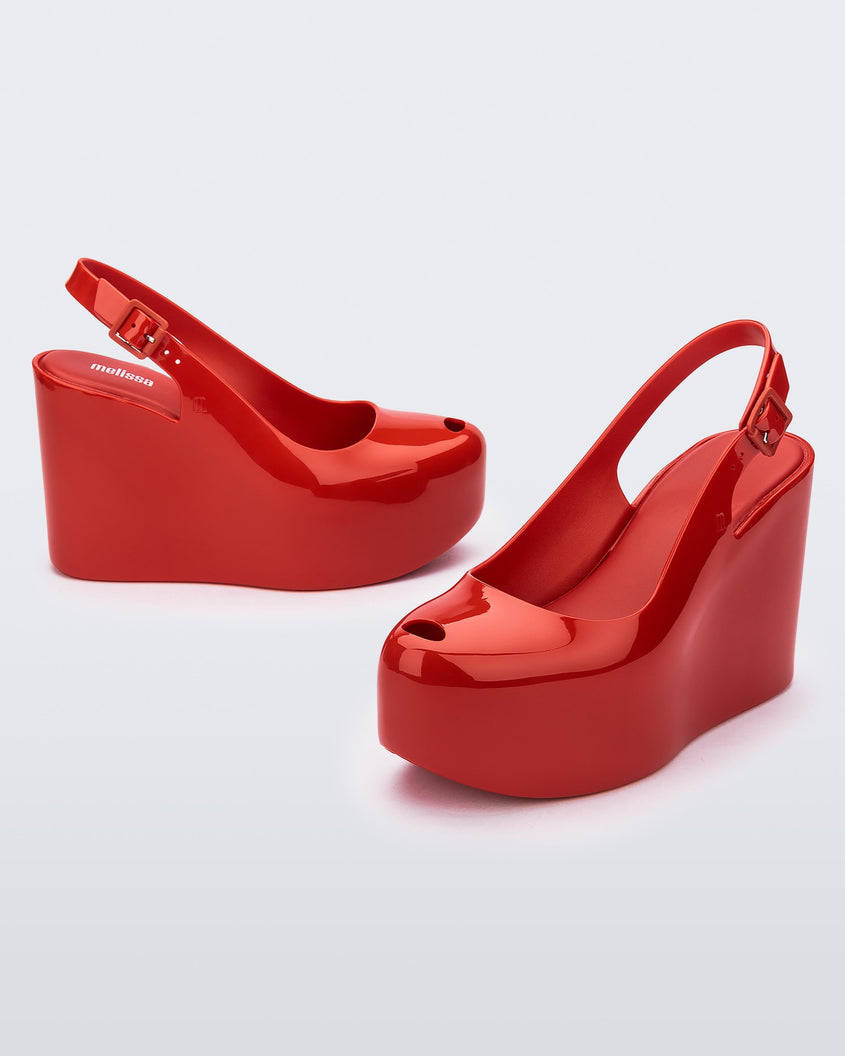 Side and angled view of a pair of red Melissa Groovy wedge platform slingback heels with peep toe.