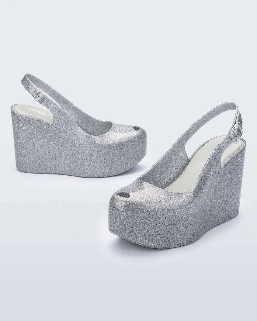 Side and angled view of a pair of clear glitter Melissa Groovy wedge platform slingback heels with peep toe.