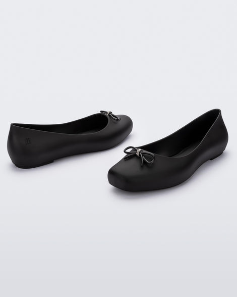 Angled view of a pair of black Melissa Aura Basic flats with a black bow.