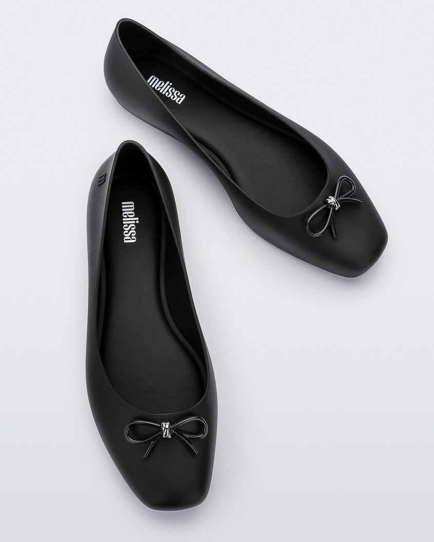Top view of a pair of black Melissa Aura Basic flats with a black bow.