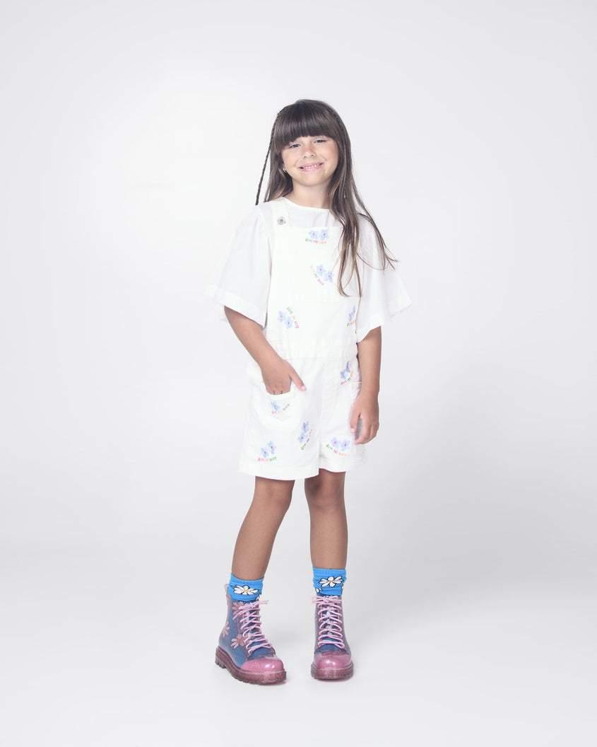 A child model in a white dress wearing a pair of glitter pink Melissa Coturno boots.
