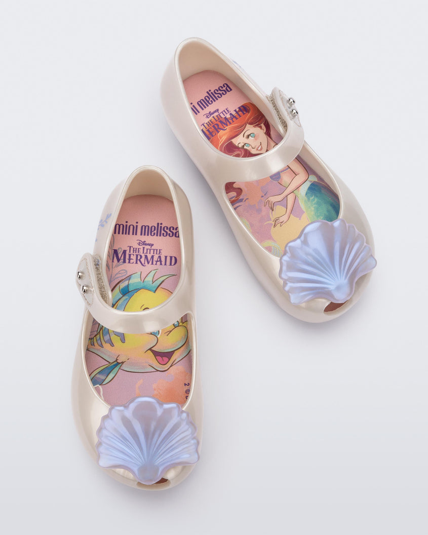 Top view of a pair of pearly white Mini Melissa Ultragirl + Disney Little Mermaid flats with pearly blue shell on top
